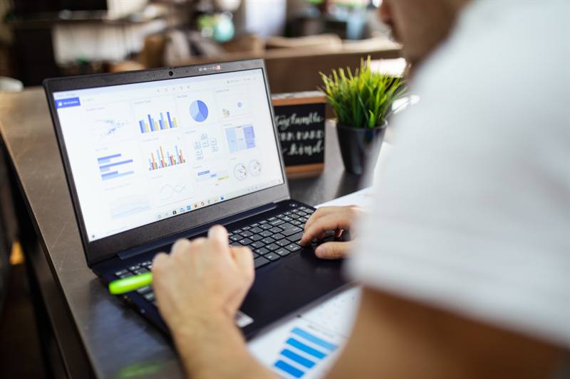 A person types on a laptop showing charts and graphs.